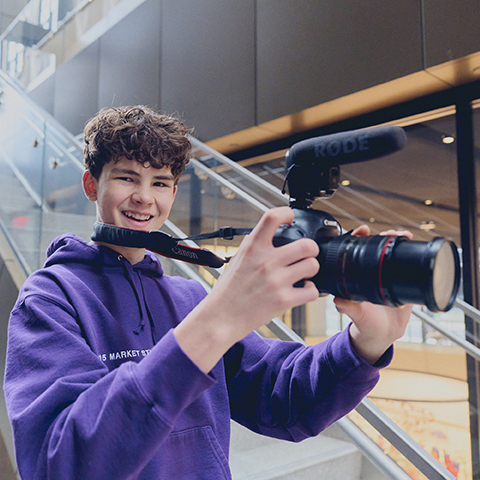 a smiling student standing with a camera stand