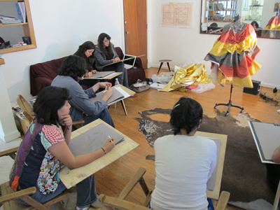 students sitting at desks sketching dress on form in front of them