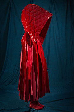 red ensemble with oversized detachable hood and cape with streamer-like panels cut from upper boduce to hem