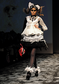 woman walking down runway wearing ruffled short dress, black tights and black boots with feathers at ankles