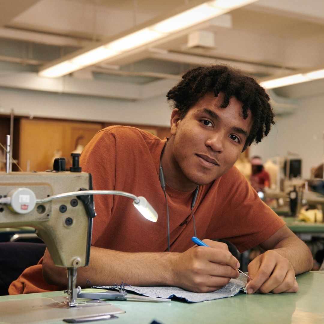 Precollege student at a sewing station, smiling at the camera