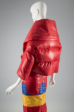 Red Sleeping Bag suit in polyester with down fill; puffer style shawl collar jacket; jeans style skirt with horizontal bands at upper skirt in blue and yellow