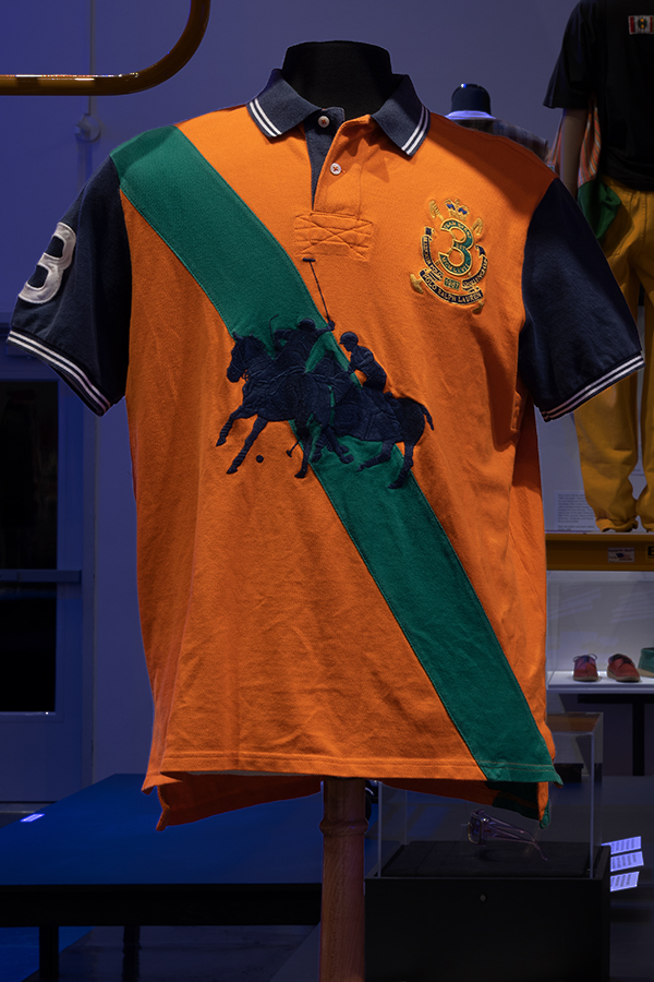 Orange short sleeve polo with silhouette of two polo riders over a diagonal green stripe
