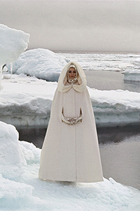 woman in full length creme cape with metallic gloves standing on iceberg