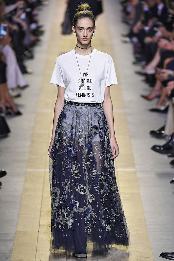 model walking down runway in sheer blue embroidered and embellished skirt and white t-shirt that read 'We Should All Be Feminists'"