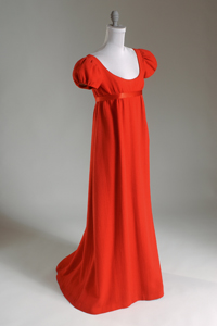 evening dress in red nubby wool crepe with satin piping and waistband extending to back ties with empire bodice, deep scoop neck, short puff sleeves anf long straightline trained skirt