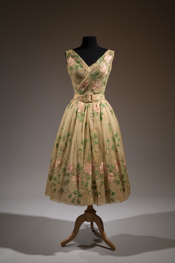 tan-colored v-neck, sleeveless dress embroidered with pink flowers and belted at the waist