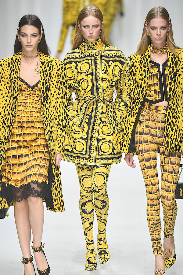three runway models walking in coordinating black and yellow patterned ensembles