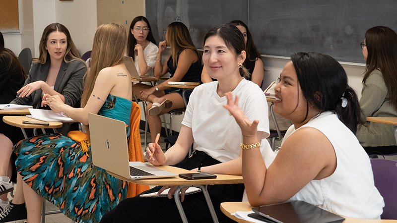 A classroom image of students at their desks conversing with each other.