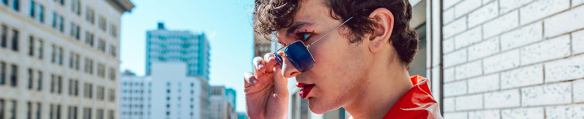 young male with red lipstick and sunglasses pulled down over his nose and looking into the distance