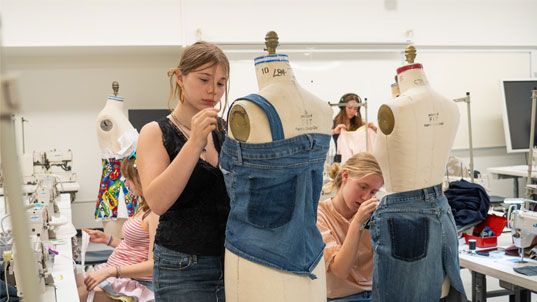 A female student standing over a dress figure working on a denim skirt