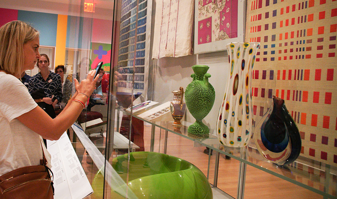 woman taking a photo of vases in an exhibit case
