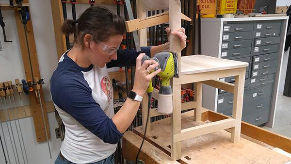 female student working with powered wood planer building a chair