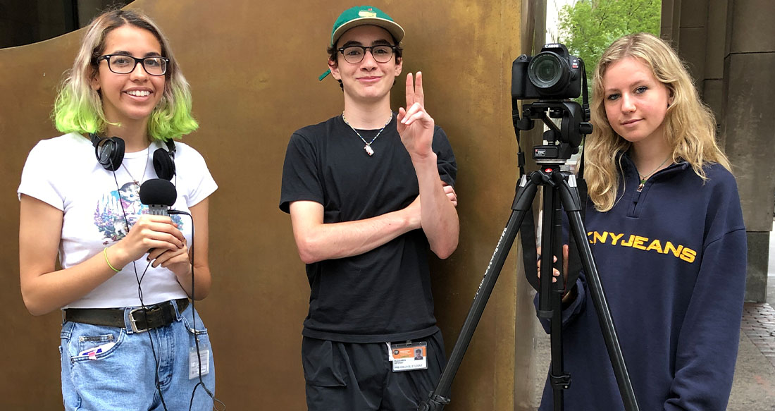 three students standing together holding filming equipment