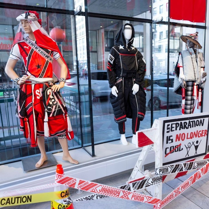 menswear featuring red, white, black materials, crossed lines and symbols with political overtones. Caution tape and road and warning signs used in the installation reinforce the sense of power and control