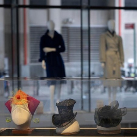 three women's hats on forms, two of black share materials and one featuring red, orange, and green elements