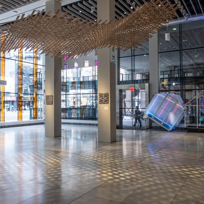 A light wood lattice hung high in the exhibition space. light passes through the structure creating a light and shadow pattern on the floorlatice