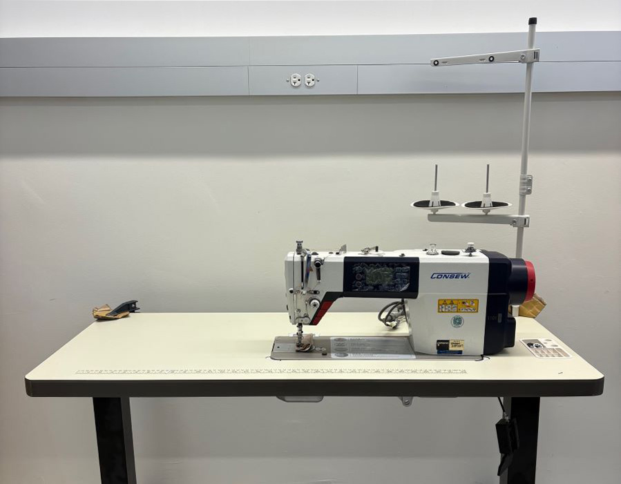 Fully hand-operated sewing machine, designed without foot pedals for accessible use, on a height-adjustable table.