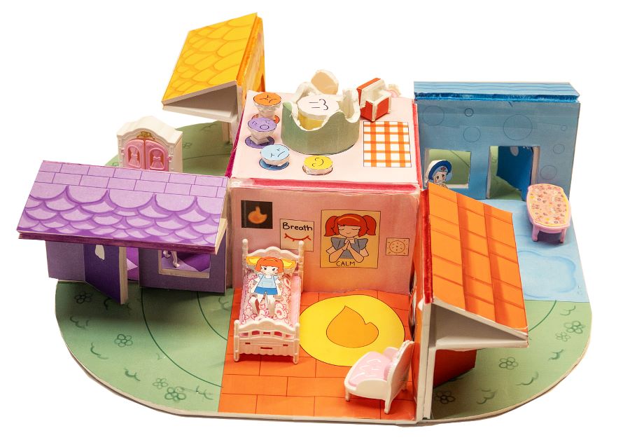 Colorful cardboard model of a dollhouse with circular connected rooms and outdoor spaces. Illustrated furniture and household items fill each room. The house is designed as an imaginative play children’s activity for learning and storytelling.