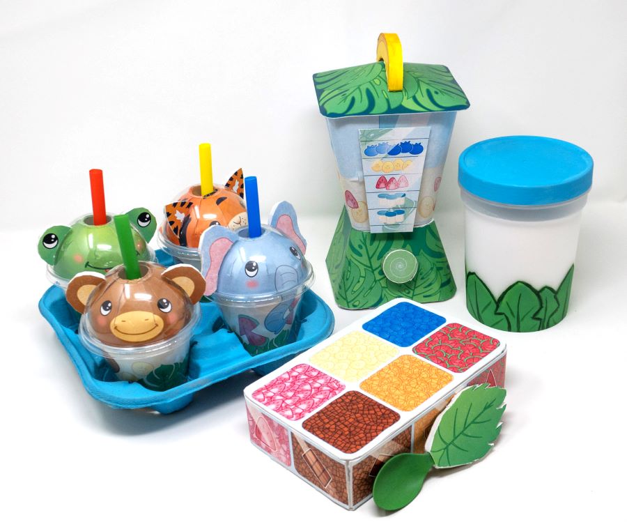 Colorful children’s imaginative play smoothie shop prototype made of paper. Displayed are four animal-faced cups with straws in a blue tray, a blender, a white container with a blue lid, and a box resembling a container.