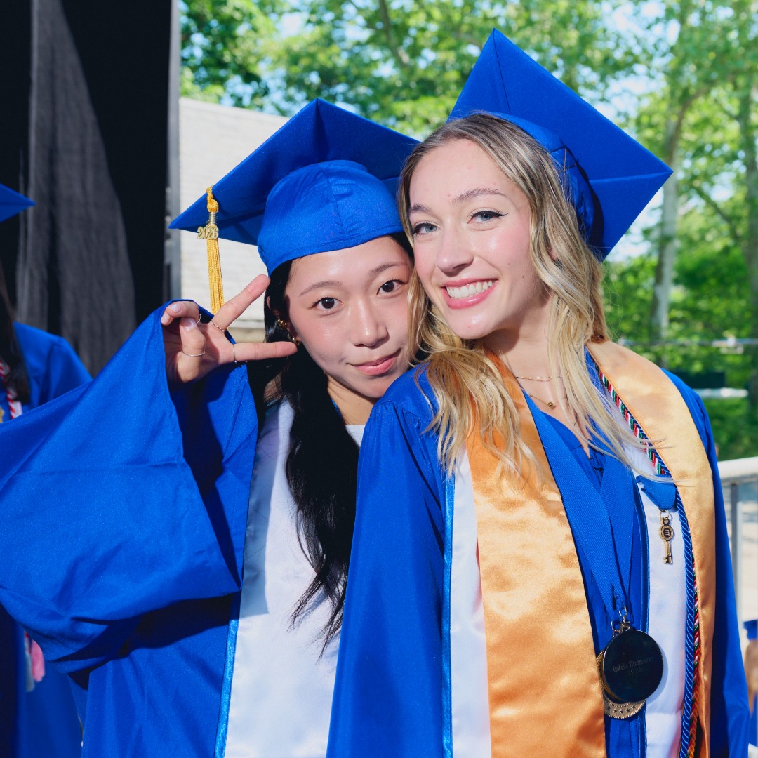 two alumna smile for a photo at 2026 Commencement.