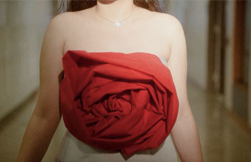 A model wearing a white dress with a red rose applicae
