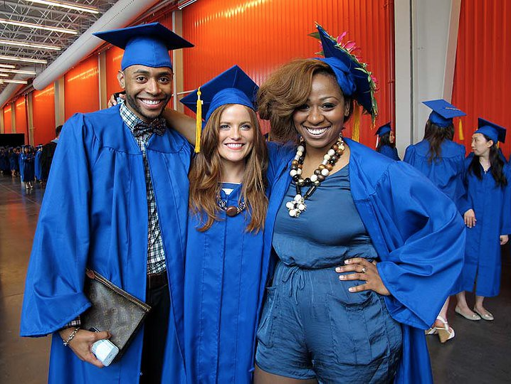 Three students in blue cap and gown with their arms around each others backs smiling