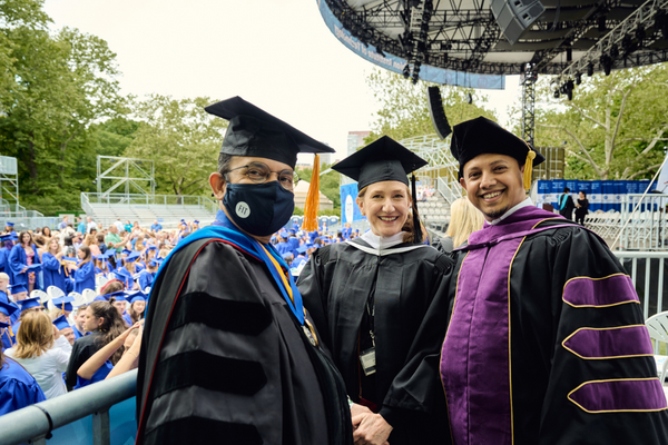 three faculty members at commencement venue with graduating students in the background