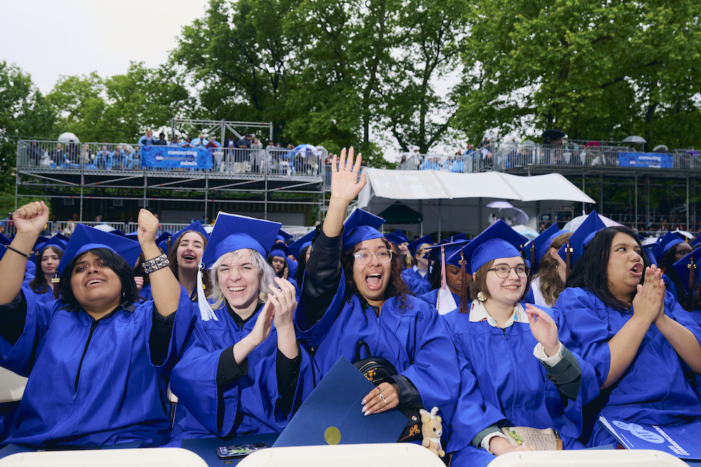 a row of students in blue regalia cheering 