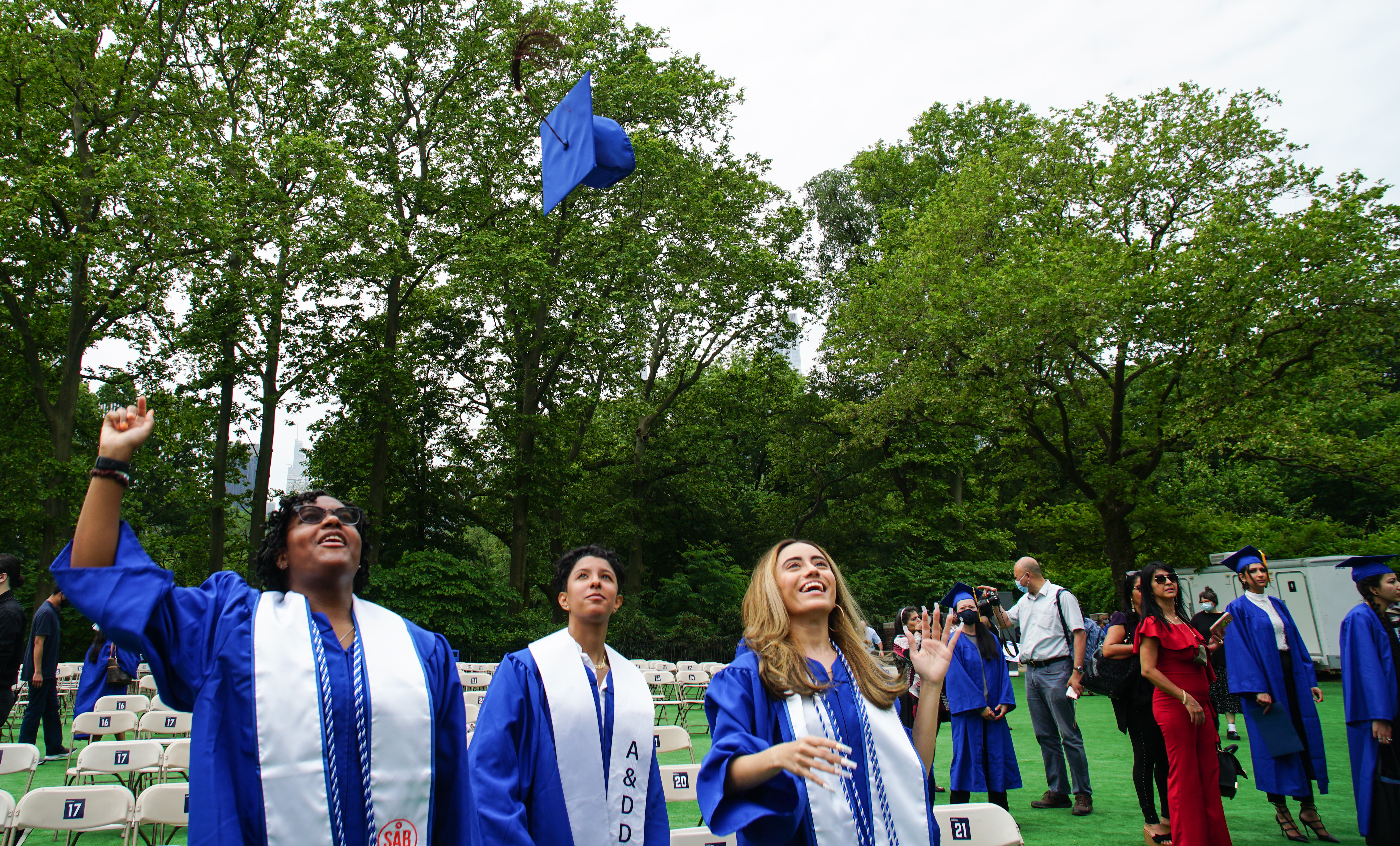 students at commencement in Central Park with mortarboard in midair 
