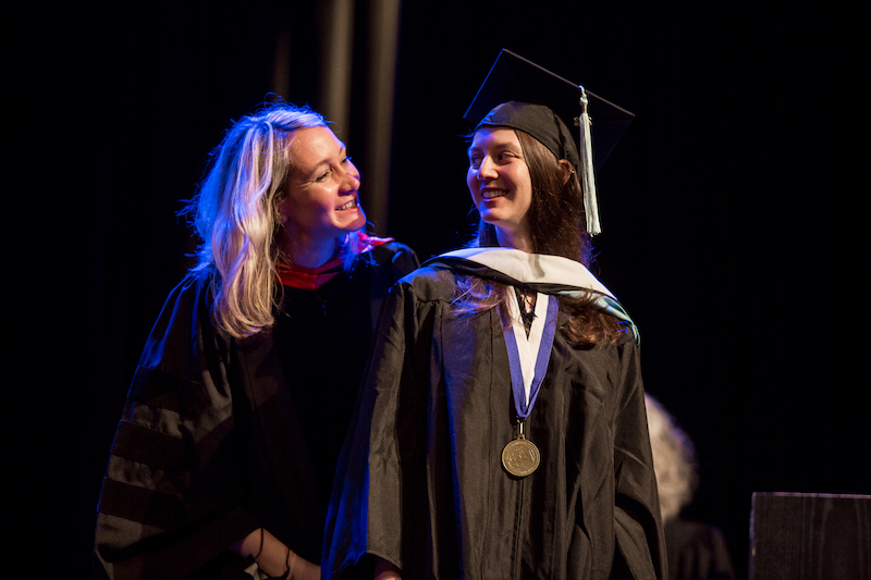 faculty member congratulating student after placing master's hood over their head
