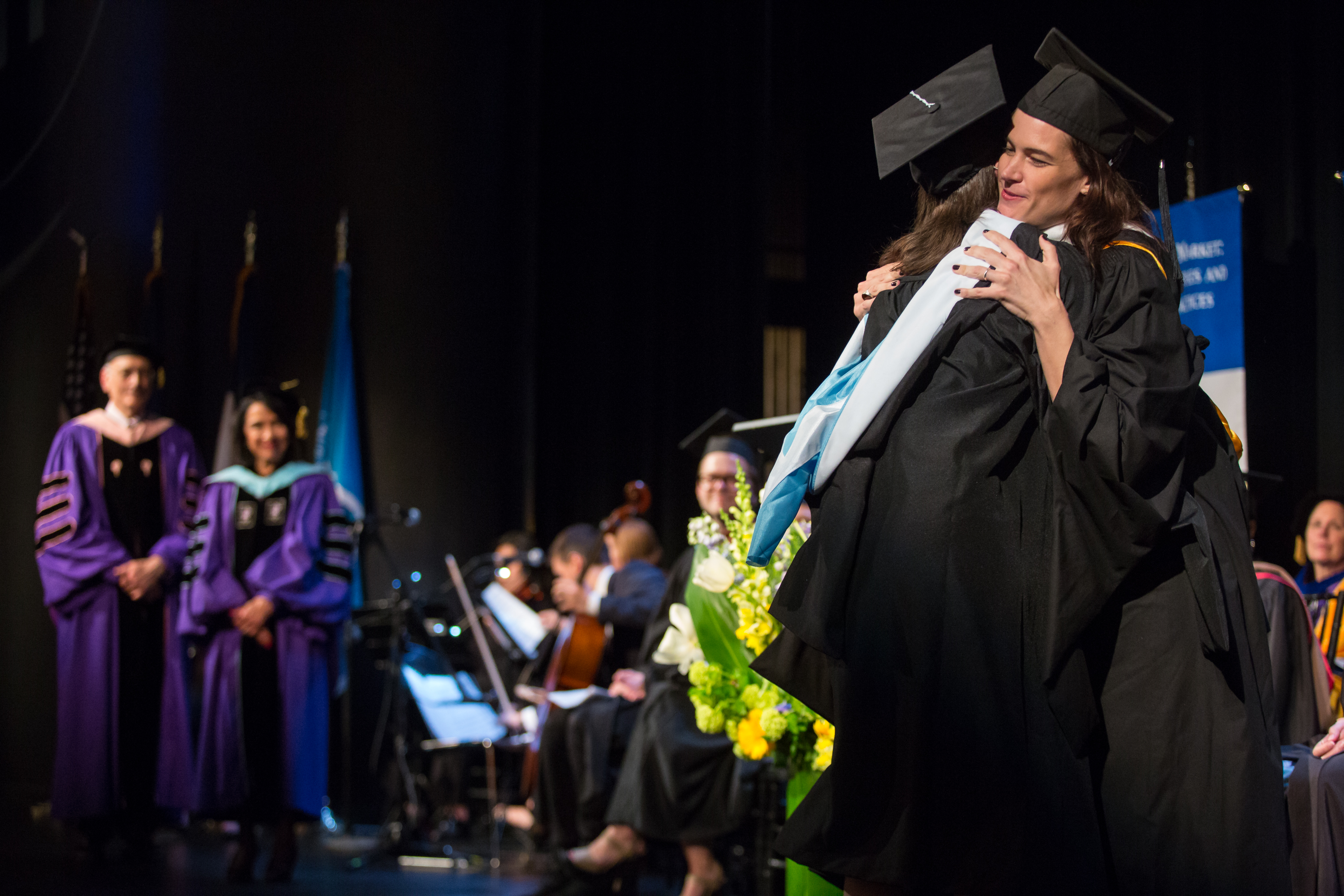 faculty member giving student a hug on commencement stage