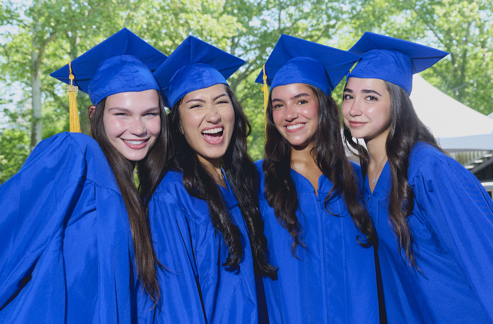 four students in blue cap and gown pose at FIT's 2026 commencement