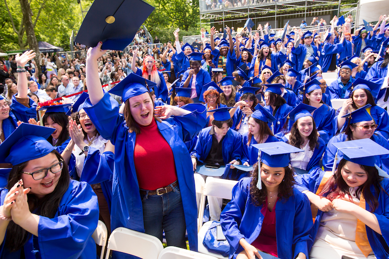 undergraduate students in the audience at commencement, one is standing and cheering