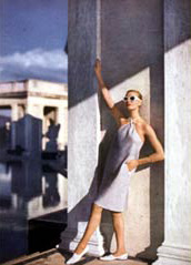 woman with white sunglasses in dress and white shoes leaning against building