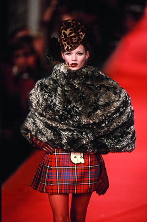 Model Kate Moss in a fur cape and tartan miniskirt on a red catwalk