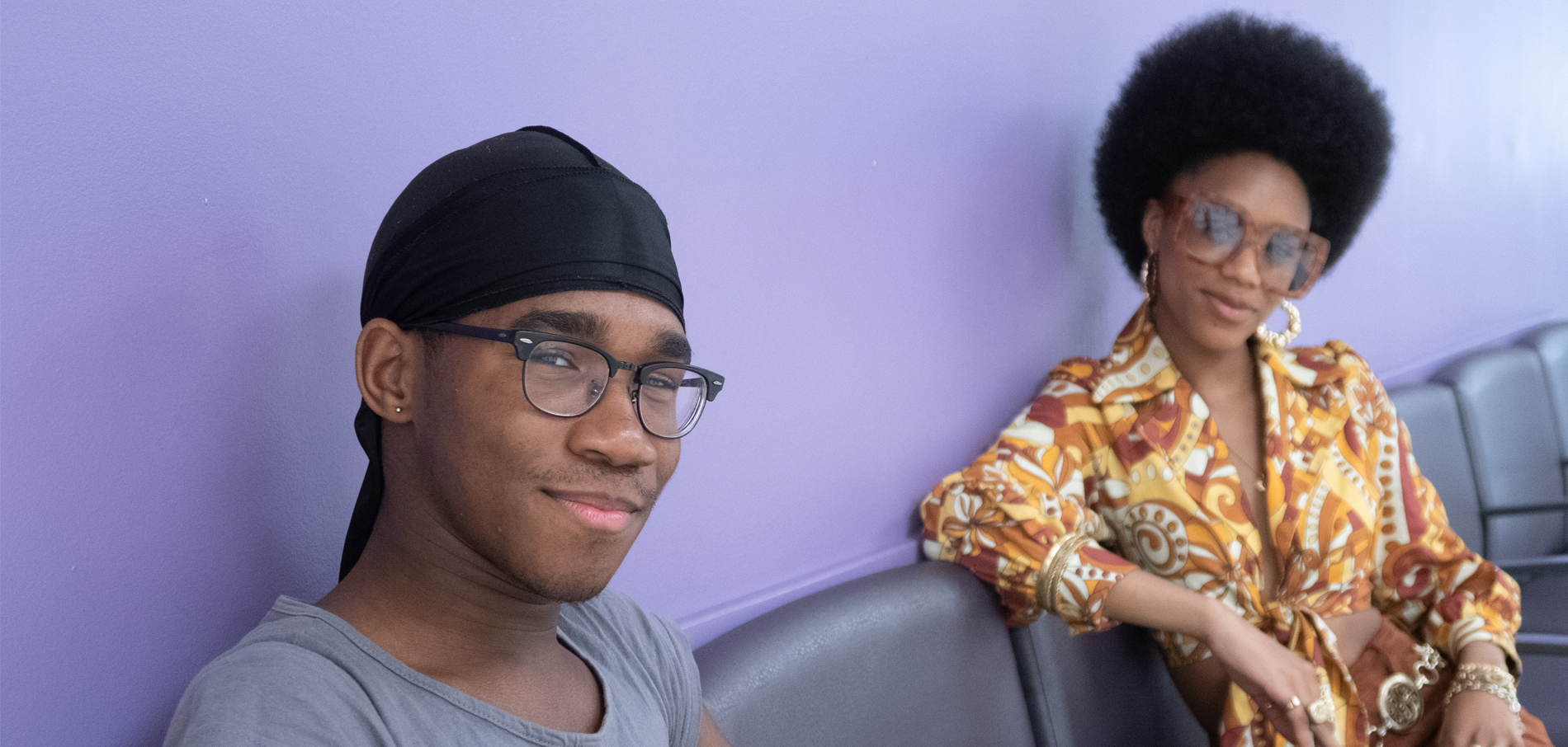 two smiling FIT students sitting in room with purple background