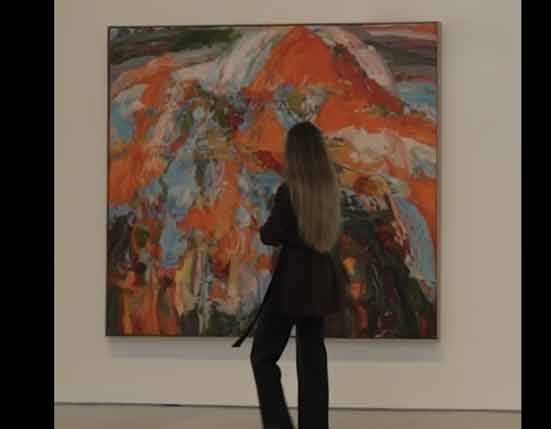 A woman with long hair standing in front of an abstract painting