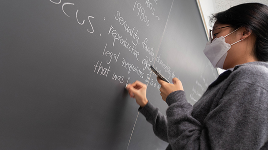FIT student in Business & Technology class writing on a blackboard