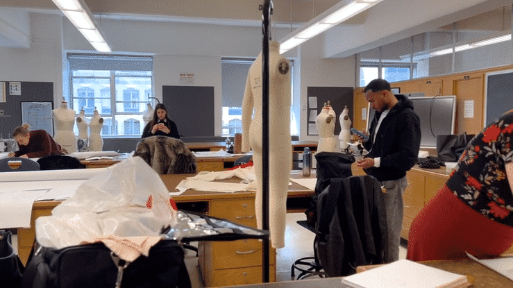 a pan of the classroom with an instructor showing a student a pattern