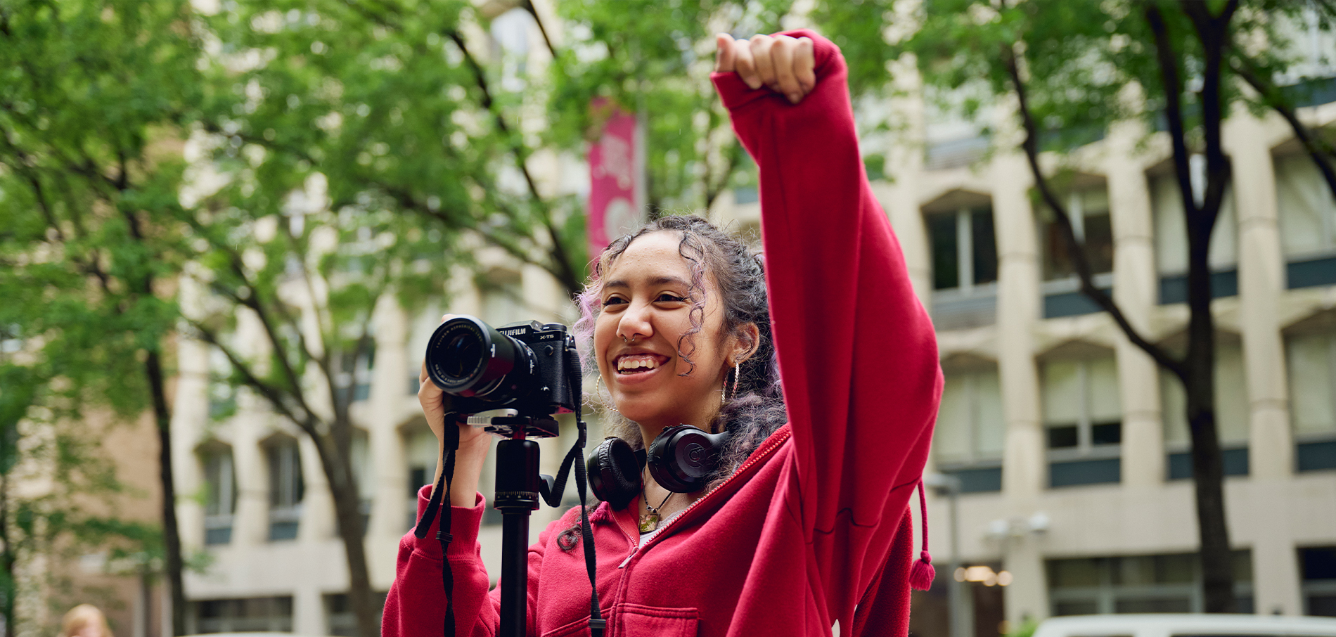FIT student holding camera with airm raised on campus