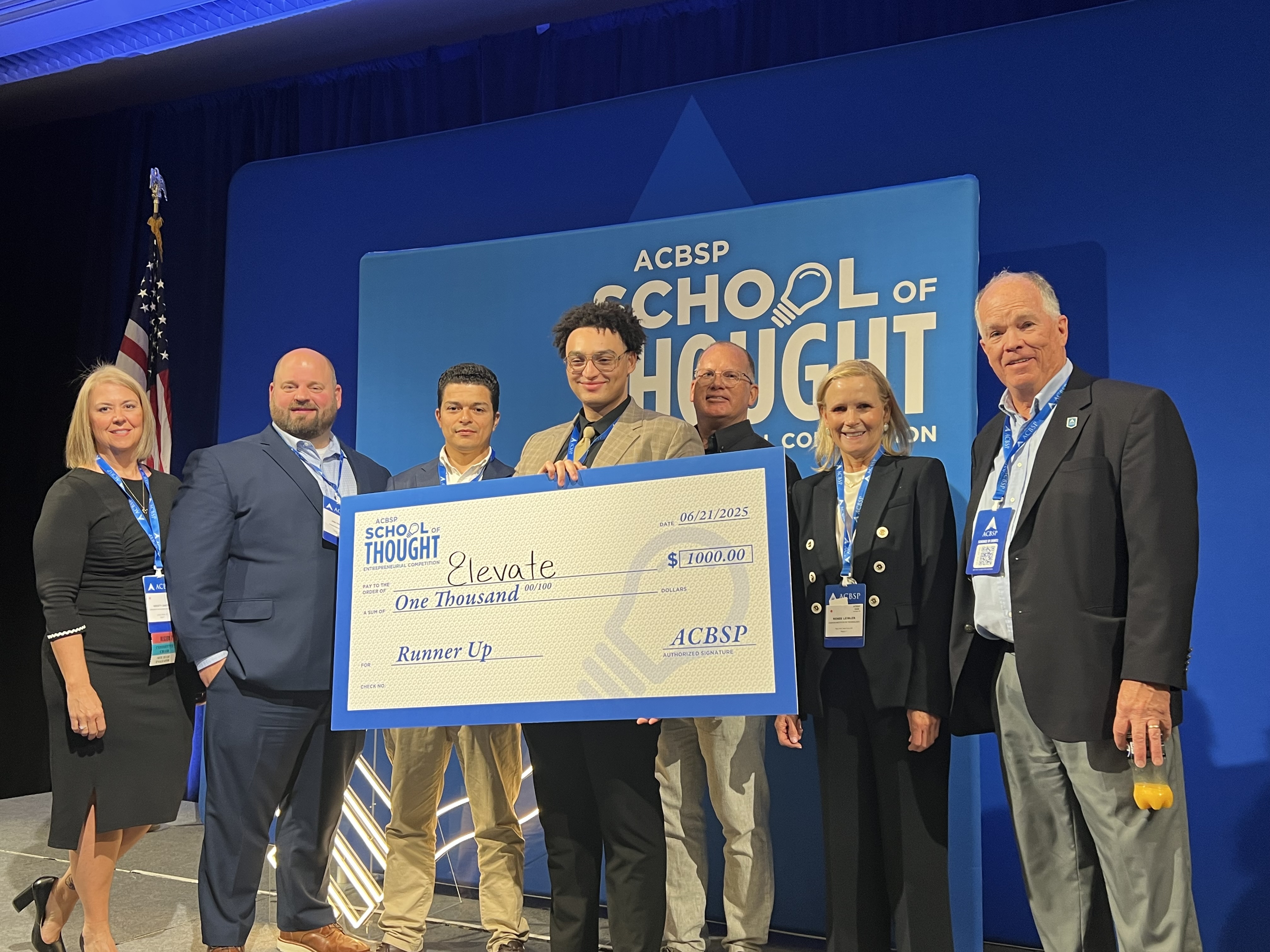 Nicholas Alexis standing with judges and holding a check for his app Elevatemedia.ai
