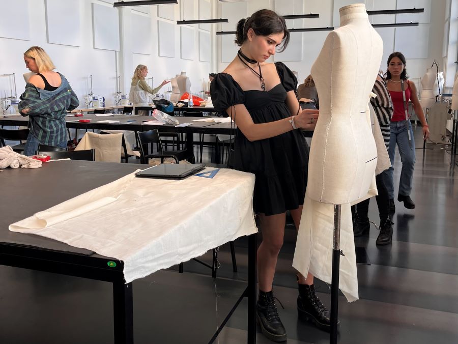 a student is draping muslin on a mannequin dress form in a fashion design classroom