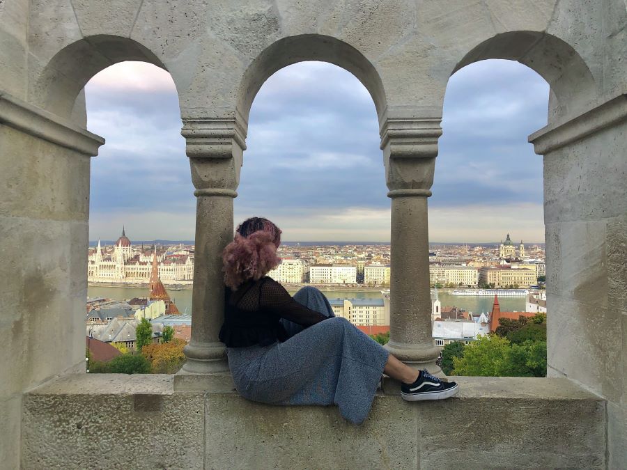 A student sitting in one of the arches of a cloistered arcade, overlooking the city and the river 