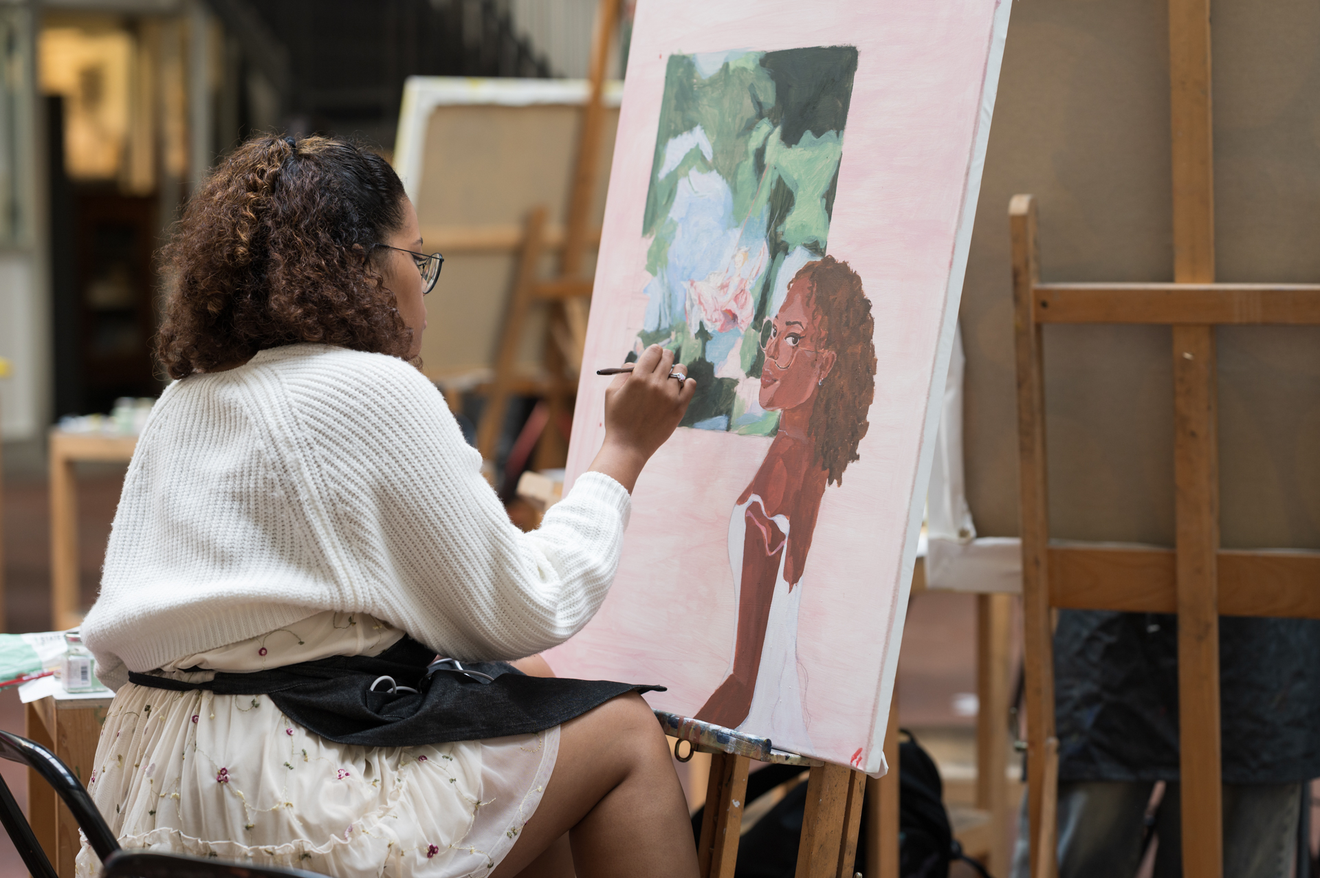A student paints a portrait in a studio, focused on her colorful canvas. Ask ChatGPT