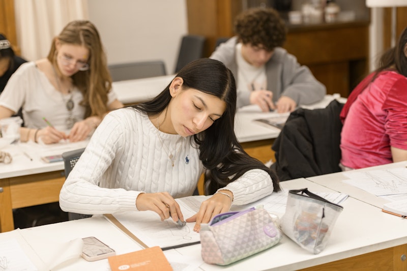 A female student at a desk drawing a sketch for a gown