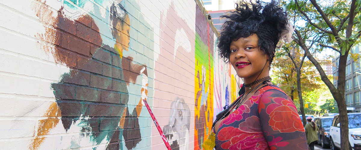 BIPOC student standing infront of illustrated wall at FIT