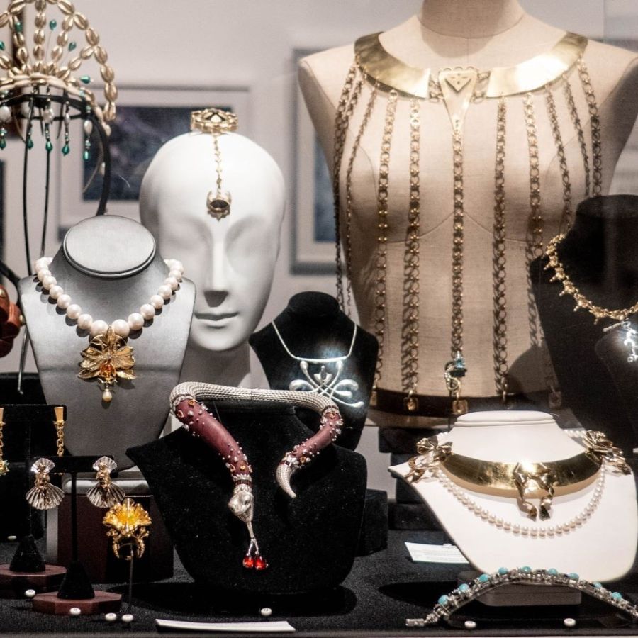 a collection of jewelry pieces - necklaces, bracelets, rings, head, and torso adornments in variety of materials, displayed in a vitrine on a variety of mounts
