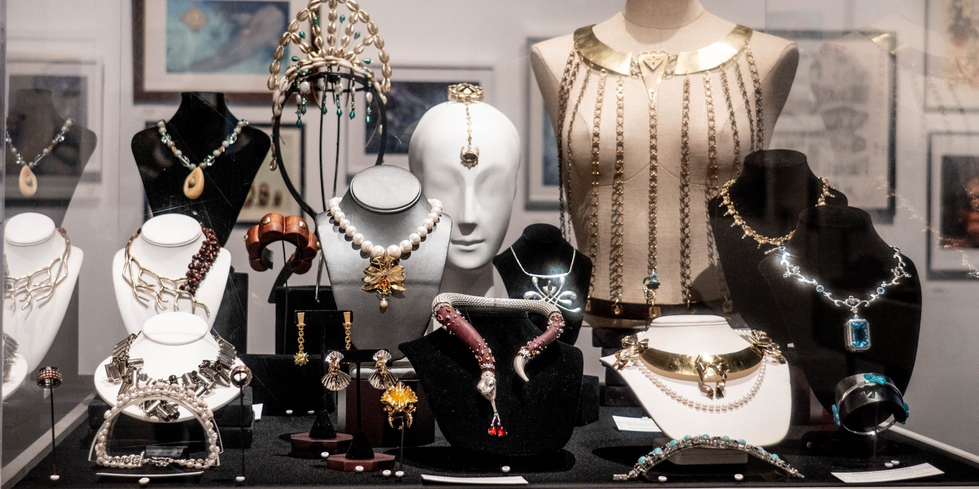 a collection of jewelery pieces - necklesses, bracelets, rings, head, and torso adornmets in variety of materialas, displayed in a vitrine on a variety of mounts