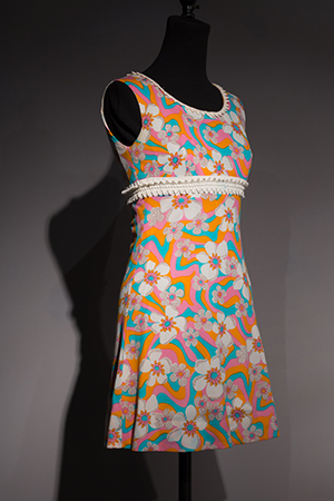 Pink mini dress with illustrated flower pattern on dress form in gallery